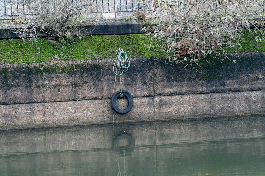 a tire is hanging on the side of a wall near a body of water